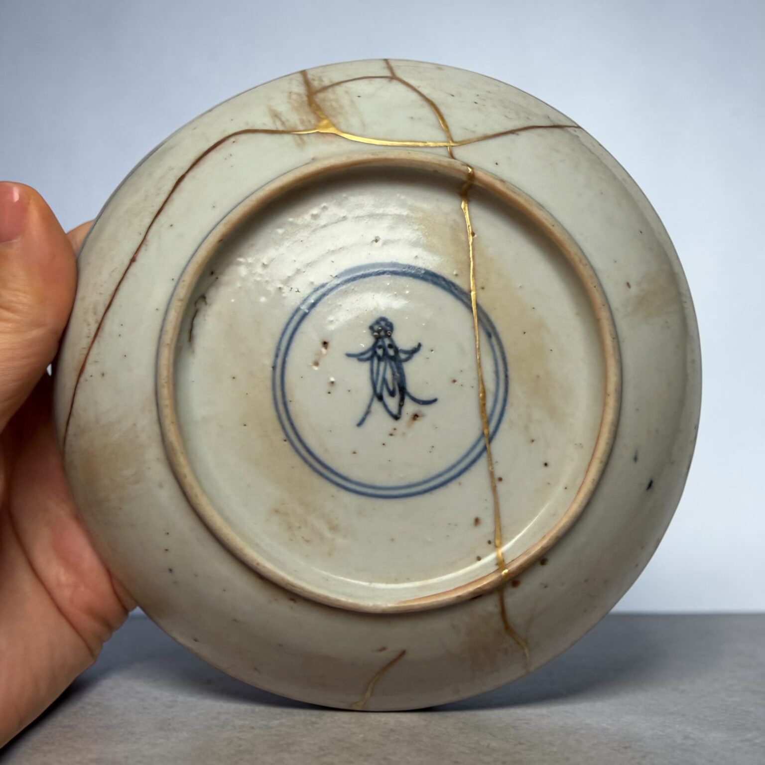 Close-up of a porcelain plate with gold-filled cracks (kintsugi) being held by a hand.