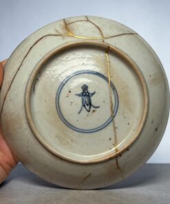 Close-up of a porcelain plate with gold-filled cracks (kintsugi) being held by a hand.