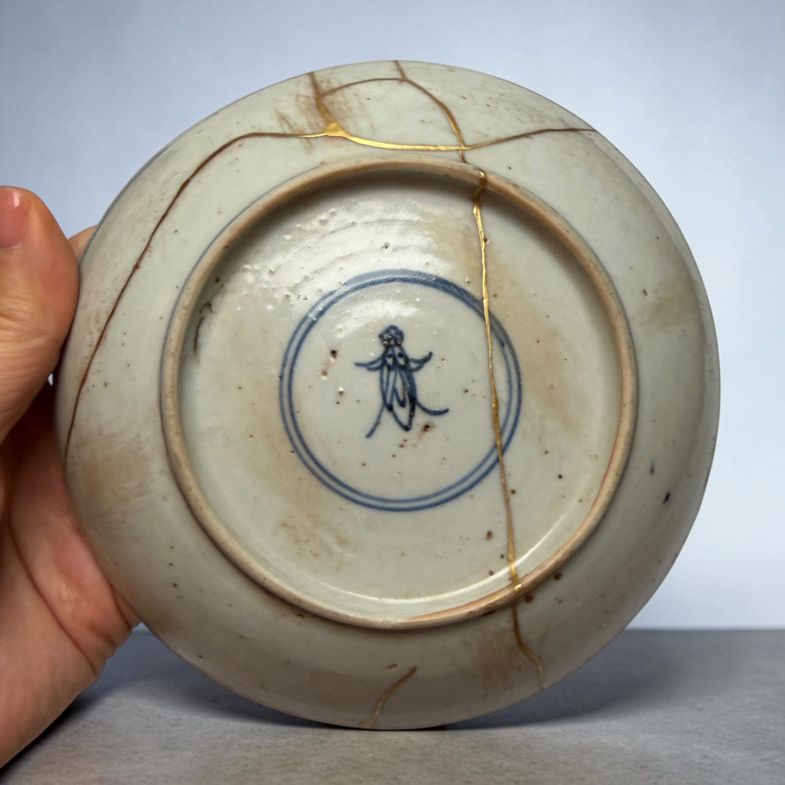 Close-up of a porcelain plate with gold-filled cracks (kintsugi) being held by a hand.