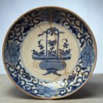 Partial view of a blue-and-white ceramic bowl with gold kintsugi repair seams running across its surface and rim.