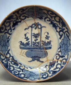 Partial view of a blue-and-white ceramic bowl with gold kintsugi repair seams running across its surface and rim.