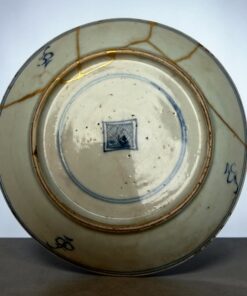 Close-up of a porcelain plate with a blue rim and gold repair lines (kintsugi) along the cracks.