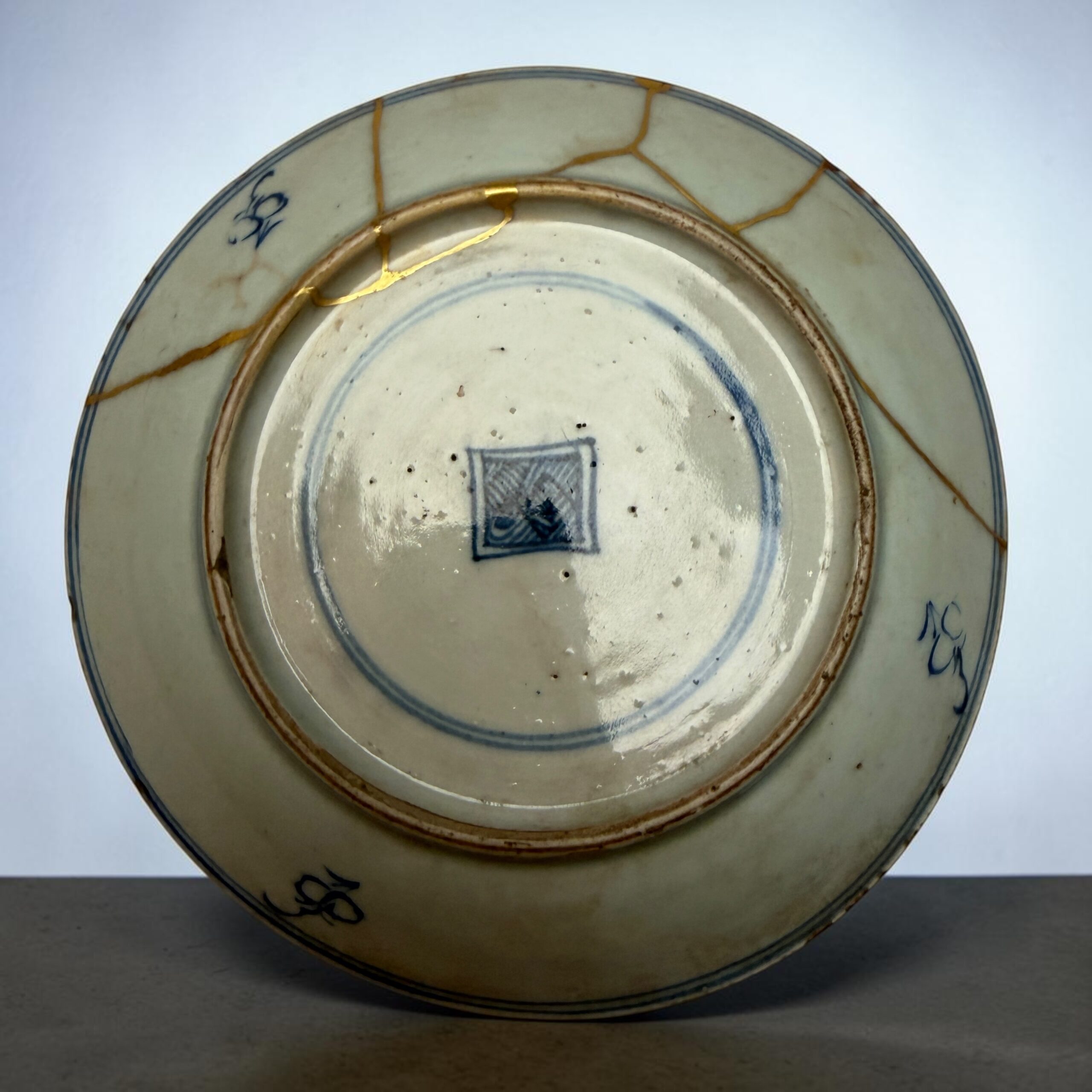Close-up of a porcelain plate with a blue rim and gold repair lines (kintsugi) along the cracks.