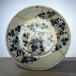 Close-up of a blue-and-white porcelain plate repaired with gold seams (kintsugi) on a gray surface.
