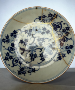 Close-up of a blue-and-white porcelain plate repaired with gold seams (kintsugi) on a gray surface.