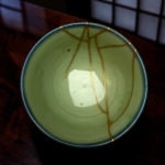 Top edge of a pale green ceramic bowl with thin gold lines, set on a dark wooden table.