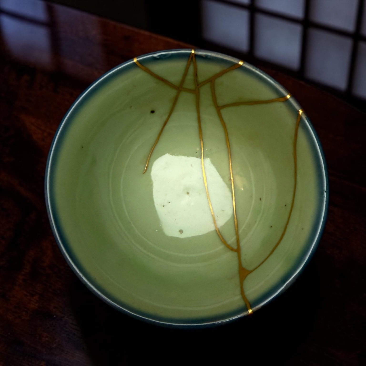 Top edge of a pale green ceramic bowl with thin gold lines, set on a dark wooden table.