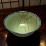 Close-up of a pale green ceramic bowl with gold decorative lines on a dark wooden table surface