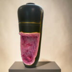 Close-up of a black, glossy sculpture with gold lines and a pink crystal base on a gray pedestal.