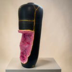 Black ceramic sculpture with a pink crystal geode insert along the base and gold seam lines, displayed on a white pedestal.