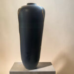 Black ceramic vase with gold crackled lines on a gray pedestal against a pale wall.