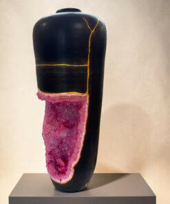 Black ceramic vase with yellow crackle glaze lines, sitting on a gray pedestal with pink crystalline material wrapped around its base, in a gallery setting.