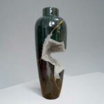 Tall ceramic vase with dark green glaze, brown base, and a white crystalline crack running down the side.