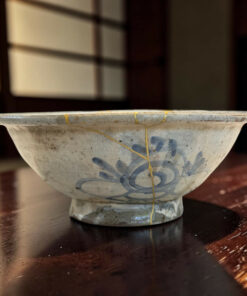 Close-up of a blue-flowered ceramic bowl resting on a dark wooden table, highlighting its glaze and worn edges.