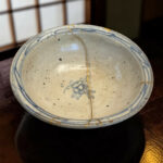 Close-up of a blue-and-white ceramic plate with a thin gold crack running across its surface on a dark wooden table