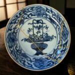 Close-up of a blue-and-white porcelain plate with gold kintsugi repairs on a wooden surface.