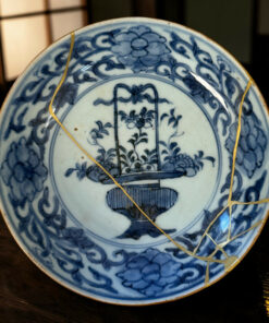 Close-up of a blue-and-white porcelain plate with gold kintsugi repairs on a wooden surface.