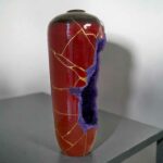 Red ceramic vase with gold repaired cracks (kintsugi) and a purple chipped area along the side.