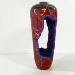 Red ceramic vase with a purple textured wrapping and gold vein patterns on a white background much of the image showing the vase edge and wrap piece.