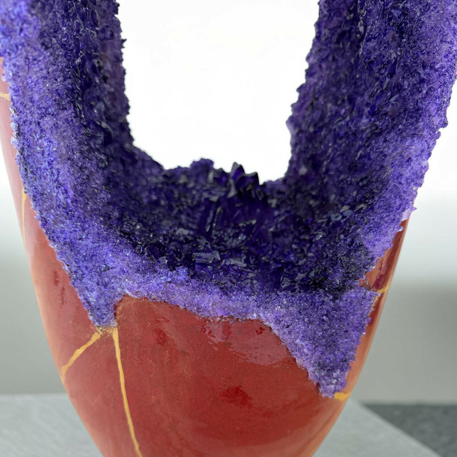 Close-up of a terracotta pot rim coated with a rough purple crystal texture.