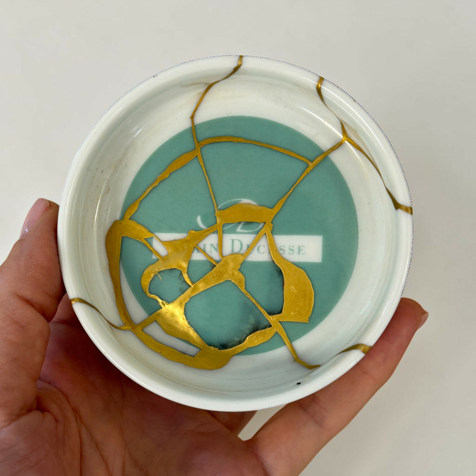 Close-up of a decorative plate with a turquoise center and gold crackle pattern, held in a hand.