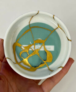 Close-up of a decorative plate with a turquoise center and gold crackle pattern, held in a hand.