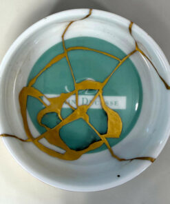 Close-up of a ceramic plate with teal center and white rim, repaired with gold cracks (kintsugi).